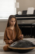 © Tatjana - Young girl playing handpan drum at home, practicing music with focus and calm mood.
