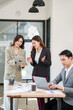 © aekachai - Group of young Asian professionals engaging in a dynamic brainstorming session. A female leader stands confidently while presenting ideas to her colleagues, showcasing a collaborative, positive