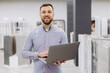 © anatoliycherkas - Man smiling, using a laptop in a showroom. He is a small business owner, sales manager, or client advisor
