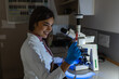 © Graphicroyalty - Smiling young female scientist examining a slide under a microscope in a dark lab, healthcare and medicine concept. Lab technician holding a sample plate for microscopic analysis and investigation.