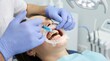 © Adil - Dentist wearing blue gloves applies a light-cured bleaching agent to the teeth of a patient using a specialized applicator tool during a whitening session.