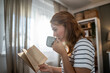 © Migma_Agency - Woman reading book and drinking coffee relaxing at home