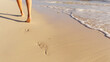 © Home-stock - Woman enjoying summer vacation by walking barefoot on sandy beach near the ocean as waves wash up, focus on footprint in the sand