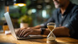 © Kateryna - Close up hourglass on wooden home office desk time measurement device with person using computer efficiency concept with deadline management shown clearly workspace environment