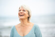 © Paula - Cheerful mature woman laughing joyfully by the sea