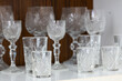 © Marek - Hand cut crystal glasses displayed on a living room cabinet shelf. Small shot glasses in front and larger wine glasses in back, detailed engraved glass made by home craftsman.