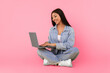 © Prostock-studio - Portrait of smiling lady using laptop computer, reading news, watching video, working or elearning remotely, sitting on floor isolated on yellow studio background wall. People And Technology Concept