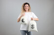 © New Africa - Happy woman holding bags with money on grey background. Dollar and euro currency symbols on fabric