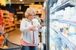 © Serhii - Woman in casual clothes shopping at supermarket store with grocery cart buy choose milk dairy produce