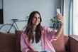 © Daniel - Happy pleasant millennial woman relaxing on comfortable couch, holding smartphone in hands. Smiling young lady taking a selfie, posting on social media, using mobile applications at home.