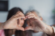 © Daniel - A happy elderly mother and her adult daughter make a heart shape with their hands while smiling at the camera, capturing a touching self-portrait that represents love, unity, and strong family bonding