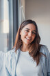 © Daniel - A confident young woman smiles naturally at the camera near a window, captured in a clean headshot portrait suitable for a professional profile, representing success, positivity, and self-assurance