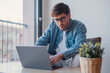 © Daniel - Young European businessman using laptop and technology apps for work or online learning, hispanic professional working at desk in office, focused on business tasks