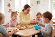© Meow Creations - Teacher in yellow sweater having lunch with toddlers at table