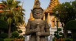 © Nyambek - Ancient statue guarding ornate temple against a bright sky background
