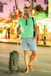© Volodymyr - Hispanic traveler on streets at night. Man traveler with a suitcase in tropical city. Summer travel in America. Traveler in the night lights city. Mature tourist with baggage. 40s traveler hold bag.