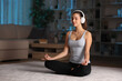 © Antonioguillem - Woman wearing headphone doing guided yoga class in the night