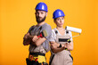 © DC Studio - Serious couple with painting tools, wearing overalls and preparing for DIY home improvement. Man poses with brush as woman holds roller, both standing confidently and ready to paint and renovate house