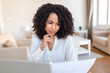 © Graphicroyalty - Business document review. Thinking woman, People in office concept. Attractive diverse female employee sitting at desk, holding a pen to her chin and looking thoughtfully at a white paper report.