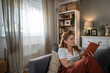 © Migma_Agency - Woman enjoying reading a book relaxing on a sofa at home