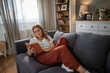 © Migma_Agency - Woman relaxing at home reading book on sofa