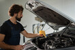 © Stockphotodirectors - A mechanic examines the oil level in a car engine using a dipstick. The workshop is well-lit, and tools are organized around him, showcasing a typical repair environment.