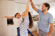 © Stockphotodirectors - A joyful family spends time together in their bright kitchen, dancing and laughing. The mother twirls with her child while the father lifts them, creating a fun and loving atmosphere.