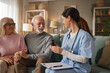 © Stockphotodirectors - Home health nurse sits with elderly couple in living room. She shows them medication while discussing their health and needs during the visit.