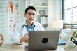 © Yingyaipumi - Professional Asian male doctor providing telemedicine service and medical consultation via laptop in a clinic. Concept of online healthcare, digital health education, and virtual physician visit.