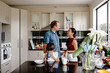 © NZstockphoto - Young girl sipping from mug in the kitchen counter while parents having a conversation behind