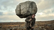 © ZaStock - Man struggles with heavy stone on back while walking through rough terrain. Cloudy sky sets moody atmosphere. Concept of construction, manual labor, determination