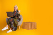 © deagreez - Glamorous mature woman with laptop sits in bright yellow studio smiling beside shopping bags showcasing casual stylish lifestyle and fashion advertising for modern retail campaigns