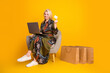 © deagreez - Glamorous mature woman using laptop holds credit card while shopping portrait in bright yellow studio with casual dress and shopping bags
