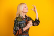 © deagreez - Elegant mature blonde woman in a patterned dress holds a coffee cup while smiling with a graceful gesture against a bright yellow background