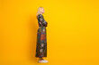 © deagreez - Mature blonde woman in a patchwork dress stands in profile yellow background stylish retro fashion confident lifestyle suitable for advertising promo