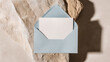 © Veronika Kraeva - Minimalistic top view of a сraft blue paper envelope placed on a white marble background. Elegant stationery mockup for invitations or greetings. Generative AI