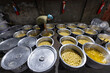 © Travel 'n' Lifestyle - Bogura, Bangladesh - 17 April 2022: View of a worker preparing a vast array of shiny, golden-syruped rasgullas in large metal pots, reflecting light in a dimly lit room.