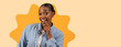 © Prostock-studio - A woman stands with a smile and a hand on her chin. She wears a casual outfit. The background has a bright color. She appears to be having a fun and light moment.