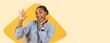 © Prostock-studio - A young woman is smiling and showing a hand gesture of approval. She is wearing a blue shirt and has a happy expression. The background features a yellow shape that enhances the joyful mood.
