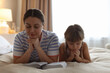 © New Africa - Mother and her daughter with Bible praying on bed at home