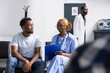 © DC Studio - Young male adult sits with healthcare professional in modern medical facility, discussing recent medical test results. Nurse uses notes on clipboard to guide patient through health insurance details.