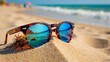 © Enigma - Sunglasses with blue reflective lenses resting in golden sand on a sunny beach, waves rolling during summer vacation