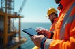 © miss irine - Worker on offshore oil rig uses tablet to check deck operations. Another engineer in hard hat supervises drilling equipment by sea. Industry professionals ensure safety.