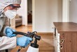 © Netsai - Pest control worker applying treatment to wooden furniture, fighting a termite infestation, professional disinfection service, indoor setting.