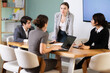 © JackF - Confident young businesswoman standing near table where sitting colleagues talking and discussing ideas in bright office