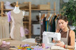 © JackF - Young female seamstress working on sewing machine with mannequin in the background. Fashion designer at work in the workshop. Ordering and tailoring clothes in the atelier