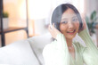© NT_studio - Happy young asian woman wearing headphones listening music while sitting on sofa with fun and enjoy in the living room at home, happiness female with entertainment, one person, lifestyle concept.