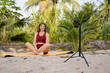 © Aleksej - Woman recording online fitness workout on smartphone in tropical outdoor setting