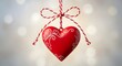 © Sikder - Red heart ornament with white swirls hanging on a red and white string