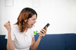 © Aphisara - Angry young woman shouting at smartphone in frustration while sitting on couch, expressing stress, anger, negative emotions in a modern home environment and daily life.